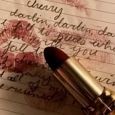 a close up of a lipstick on top of a piece of paper with writing in the background