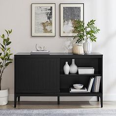 a black cabinet with plants and vases on it in front of a white wall