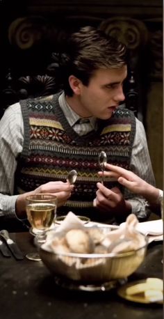 a man sitting at a table in front of a bowl of food and drinking wine