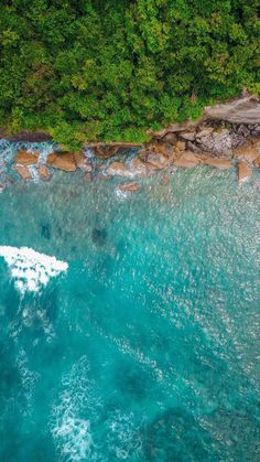 an aerial view of the ocean with rocks and green trees in the background, taken from above