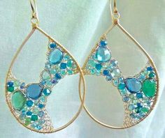 a pair of gold earrings with blue and green stones on the inside are hanging from wire