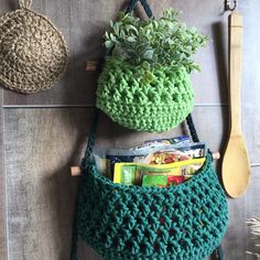 a green crocheted purse hanging on the wall next to a wooden spoon and utensil