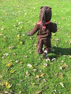 a small child in a brown bear suit running through the grass