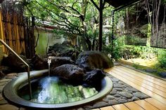 an outdoor hot tub surrounded by rocks and trees in a backyard area with wood flooring