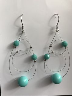 two pairs of earrings with turquoise beads hanging from the ends of hoops on a white background