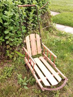 a wooden swing chair sitting in the grass next to a bush and shrub covered fence