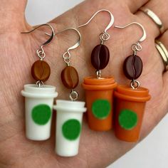 a person is holding some coffee earrings in their left hand and three cups on the right