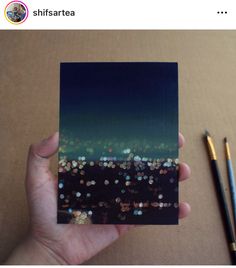 a person holding up a piece of black and white paper with city lights in the background