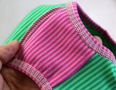 someone is stitching the side of a pink and green striped shirt with a string