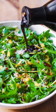 a white bowl filled with green vegetables and sauce being poured into the salad in it