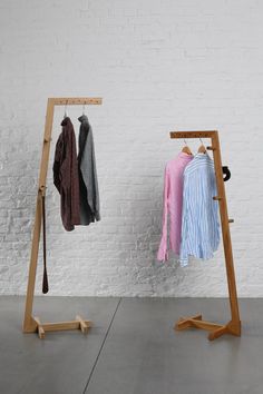 two clothes hanging on wooden racks in front of a white brick wall