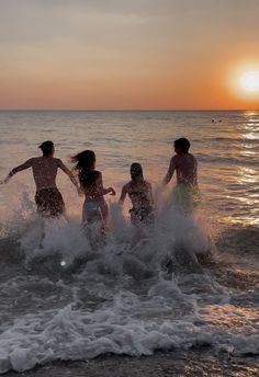 four people are playing in the ocean at sunset