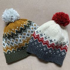 two knitted hats with pom - poms sitting on top of each other