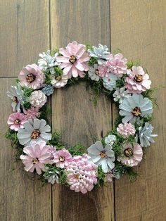 a wreath made out of pink and blue flowers on a wooden floor with grass around it