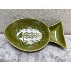 a green fish shaped dish sitting on top of a marble countertop next to a wall