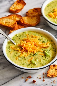 two bowls of broccoli cheese soup on a marble table with toasted bread