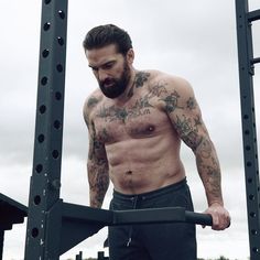 a shirtless man with tattoos on his chest holding a barbell