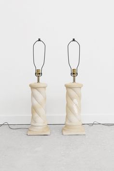 two white ceramic lamps sitting next to each other on top of a cement floor in front of a white wall