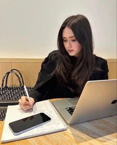 a woman sitting at a table with a laptop and cell phone in front of her