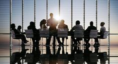 silhouettes of people sitting at a table in an office setting with the sun behind them