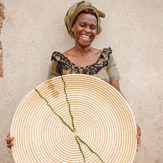 a woman holding a large woven basket with green thread on the bottom and smiling at the camera