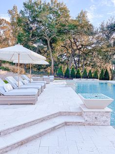 an outdoor swimming pool with lounge chairs and umbrellas next to it, surrounded by trees