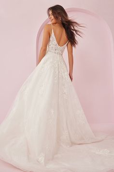 a woman in a white wedding dress standing against a pink wall with her back to the camera