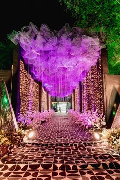 an outdoor walkway decorated with purple lights and flowers