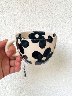 a hand holding a black and white coffee cup with flowers on the outside, in front of a white wall