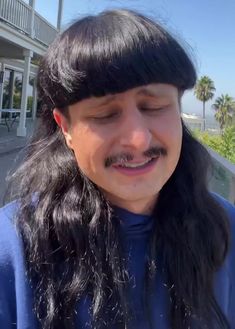 a man with long black hair wearing a blue shirt