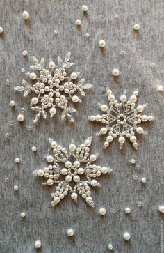 three snowflakes with pearls and beads on a gray cloth covered in white thread