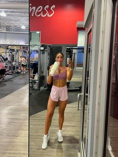 a woman holding a bottle in her right hand and standing next to a gym machine