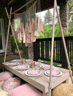 an outdoor table with plates and pink napkins on it, hanging from the ceiling