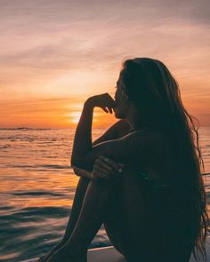 a woman sitting on top of a boat in the ocean at sunset with her hand under her chin