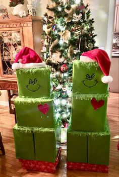 two green boxes with faces on them sitting in front of a christmas tree