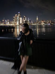 a woman is walking on the sidewalk in front of a cityscape at night