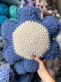 a hand holding a blue and white crocheted teddy bear in front of many balls of yarn