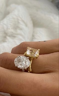 a woman's hand holding an engagement ring with two diamonds on it and a white furnishing in the background