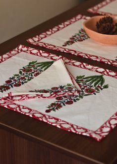 two placemats with holly and pine cones on them sitting on a wooden table