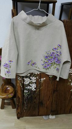 a white sweater with purple flowers is hanging on a wooden rack next to a chair