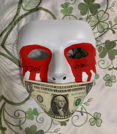 a white mask with two red eyes and one dollar bill