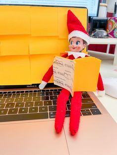 an elf sitting on top of a laptop computer holding a piece of paper in front of it