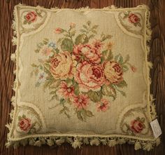 an embroidered pillow with flowers on it sitting on top of a wooden floor next to a pair of scissors