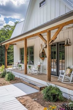 a white house with wooden porches and chairs on the front porch, surrounded by trees