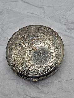 an old silver metal box with designs on it sitting on a sheet of white paper