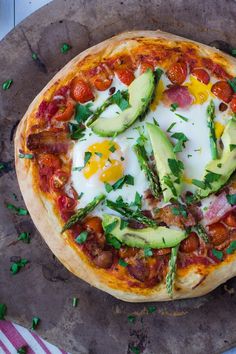 a pizza with asparagus, tomatoes, avocado and other toppings