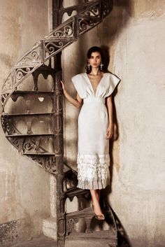 a woman in a white dress standing next to a spiral stair case with her hands on her hips