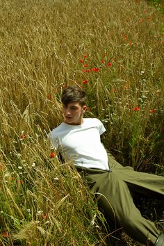 a young man laying in the middle of a field of tall grass and wildflowers