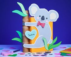 a koala bear is sitting on top of a wooden block with leaves and hearts