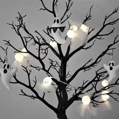 a tree with halloween decorations on it and ghost lights hanging from the branches in front of it